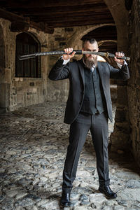 Full length portrait of man holding sword standing in corridor