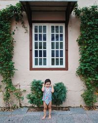 Portrait of cheerful boy standing against window amidst creeper plants