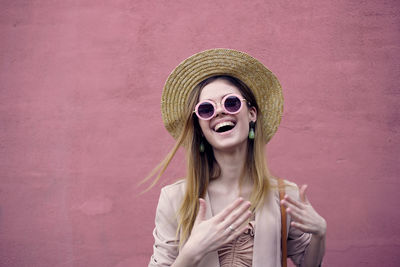 Young woman wearing sunglasses standing against pink wall