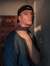 Portrait of young man looking away while standing against wall