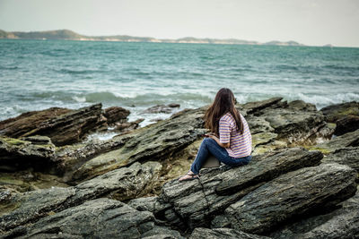 Woman sitting on rock by sea