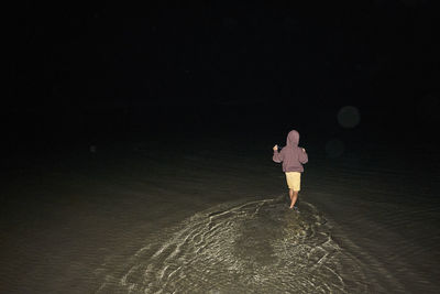 Rear view of woman standing on beach at night