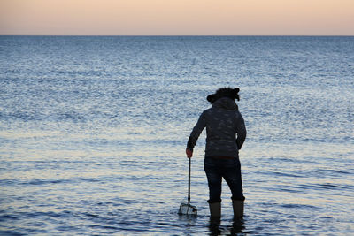 Rear view of man standing at sea shore against sky