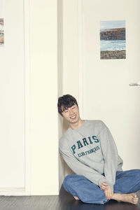 Portrait of smiling mid adult woman sitting against door