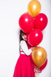 Rear view of girl holding balloons against white background