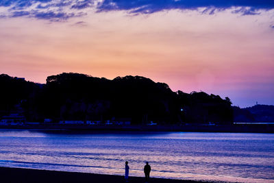 Silhouette people on beach against sky during sunset