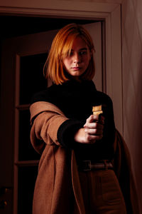 Young woman looking away while holding gun at home