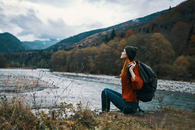 Side view of man sitting on mountain against sky