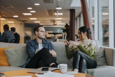 Businesswoman gesturing while discussing with young businessman sitting on sofa in office