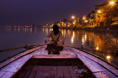Woman sitting on pier at river against sky at night