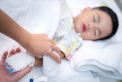 Cropped hands of mother holding sick son hand on bed