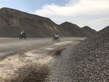 People riding bicycle on road against sky