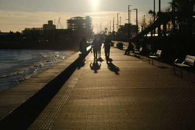 People walking on road in city against sky during sunset