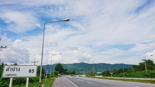 Road sign by street against sky