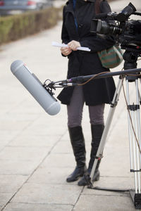 Low section of journalist standing by television camera on footpath