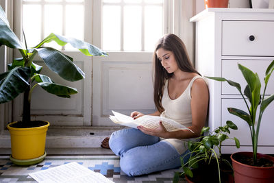 Young woman sitting on potted plant at home