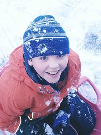 Portrait of smiling boy siting in sled on snowy field