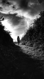 People walking on field against cloudy sky