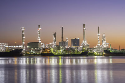 Illuminated factory by river against sky at night