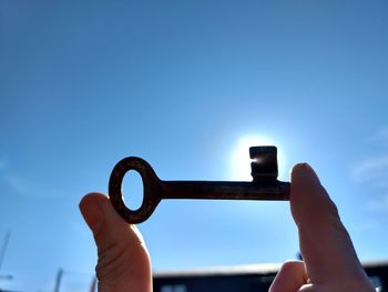 Close-up of hand holding old key against blue sky