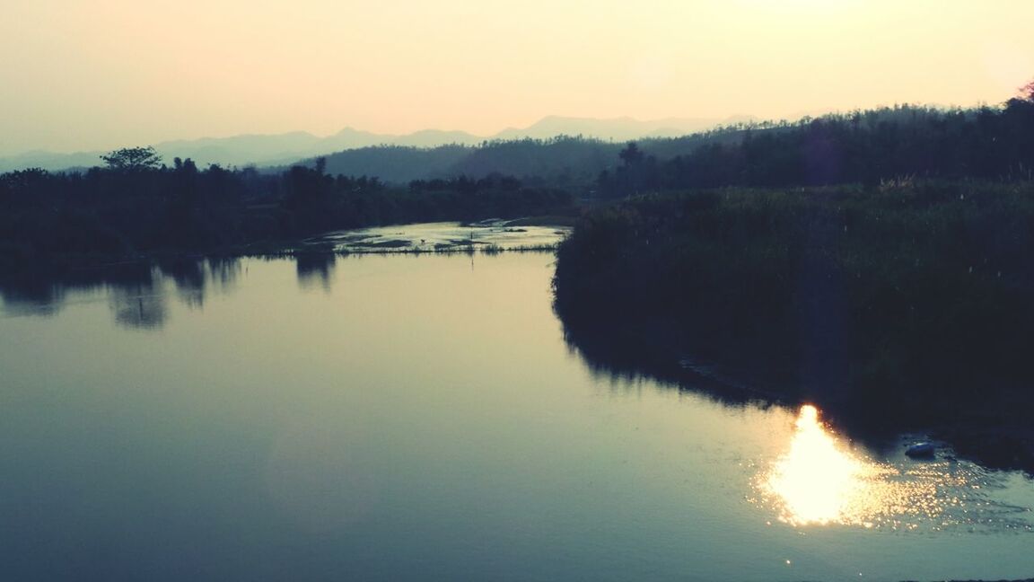 water, sunset, reflection, tranquil scene, tranquility, scenics, lake, beauty in nature, waterfront, tree, nature, sun, silhouette, idyllic, river, sky, mountain, clear sky, orange color, outdoors