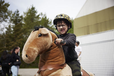 Portrait of boy having fun riding horse on wheels outdoors