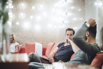 Businessman sitting with coworker while using laptop on sofa in creative office