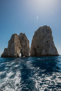 Rock formations in sea against clear blue sky