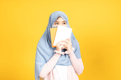 Portrait of mature man holding smart phone against yellow background