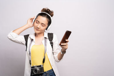 Young woman listening to music through headphones while standing against white background