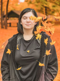 Portrait of young woman standing outdoors in the fall with falling leaves