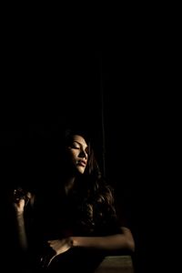 Young woman looking away while sitting against black background