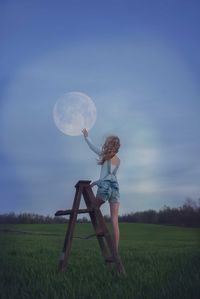 Rear view of girl touching moon while standing on ladder
