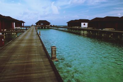 Pier amidst sea and houses against sky