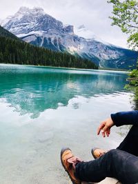 Low section of man sitting by lake against mountain