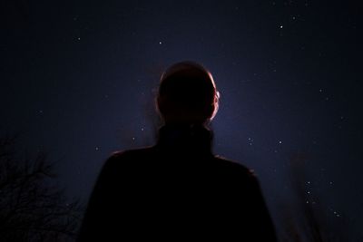Rear view of silhouette man standing against dark sky
