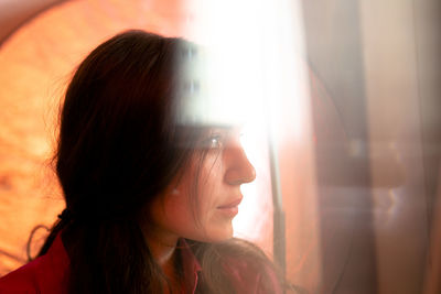 Close-up portrait of young woman looking through window