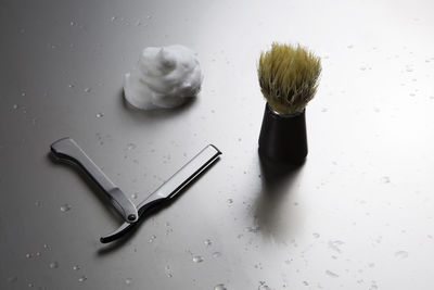 High angle view of razor with shaving brush and cream on wet table