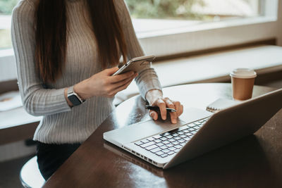 Midsection of woman using mobile phone while sitting on table