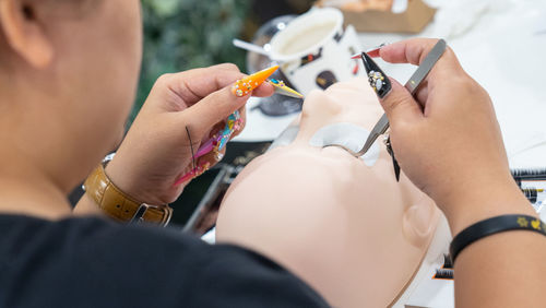 Midsection of woman applying eyelash on mannequin