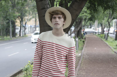 Young woman standing by road against trees