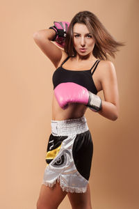 Portrait of young woman with boxing gloves over beige background