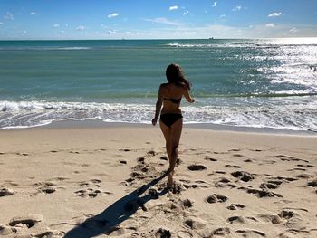 Rear view of young woman running towards sea at beach against sky