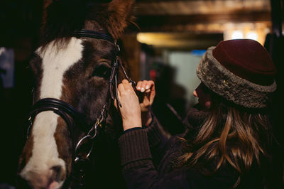 Woman adjusting horse bridle while standing outdoors at night