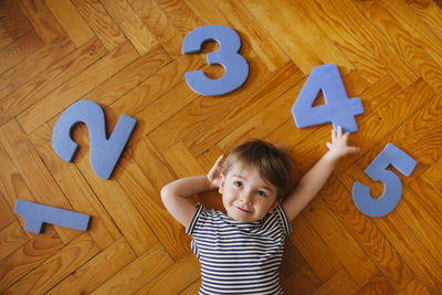 High angle view of cute boy with numbers lying on hardwood floor