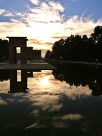 Reflection of silhouette trees in calm lake against orange sky