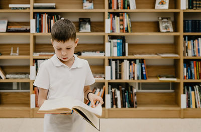 A boy stands in the library and reads a book while standing. preparing for homework. 