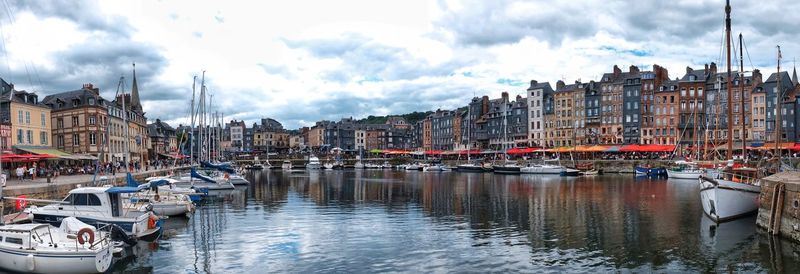 Sailboats moored on canal amidst buildings in city against sky