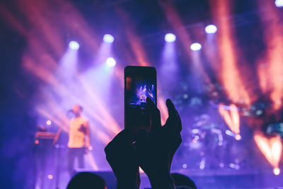 Cropped hand photographing music concert at night