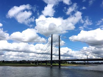 Suspension bridge over river against cloudy sky